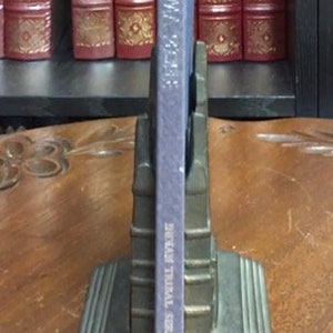 May include: A blue hardcover book titled "The Mystery of the Yellow Room" by Gaston Leroux. The book is standing upright on a pair of bronze bookends.