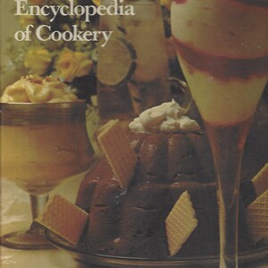 May include: A close-up of a cookbook titled "Woman's Day Encyclopedia of Cookery". The cookbook is open to a page with a photo of a chocolate dessert topped with whipped cream and surrounded by wafer cookies. There are two glasses of dessert in the background.