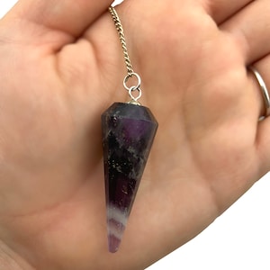 May include: A purple amethyst crystal pendulum with a silver chain. The crystal is faceted and has a pointed tip.
