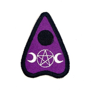 May include: A purple Ouija board patch with a black border. The patch features a black circle at the top, a white pentagram, and two white crescent moons. The patch is triangular in shape.