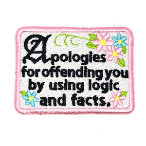 May include: Embroidered patch with a pink border and the text "Apologies for offending you by using logic and facts." Features floral accents in pink, blue, and green. The patch is rectangular.