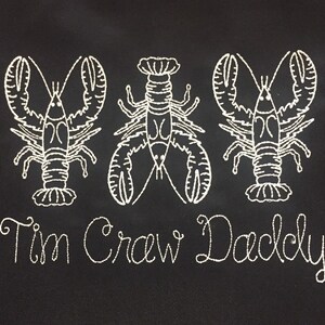 May include: Black fabric with three white embroidered lobsters and the text "Tim Crew Daddy" below.