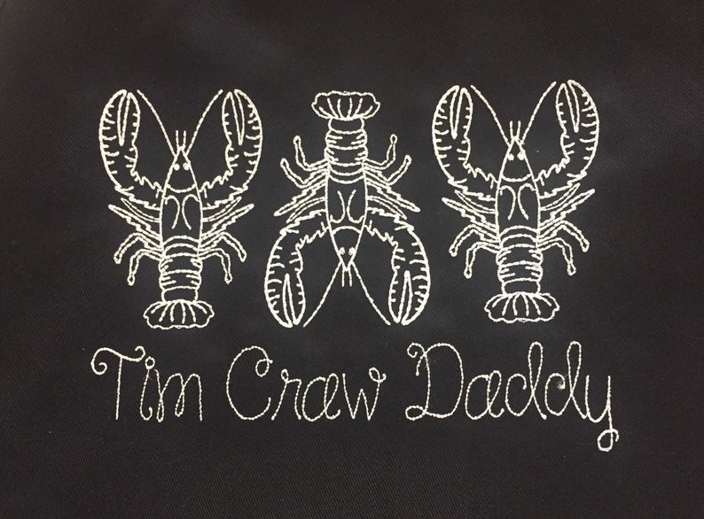 May include: Black fabric with three white embroidered lobsters and the text "Tim Crew Daddy" below.