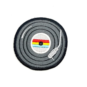 May include: A gray vinyl record with a rainbow colored label and a white needle. The record is embroidered on a black fabric patch.