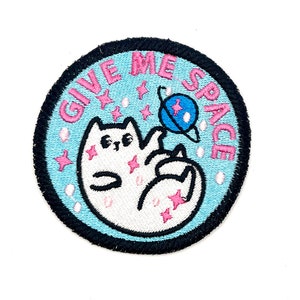 May include: A blue and white embroidered patch with a white cat holding a blue planet and the text "GIVE ME SPACE" in pink.