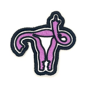 May include: Purple embroidered patch of a uterus with a middle finger raised in the air. The uterus is outlined in black.