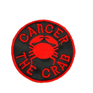 May include: Round black patch with red embroidered text and a crab graphic. The text reads "CANCER THE CRAB" in a circular pattern around the crab. The patch has a red border and is set against a white background.