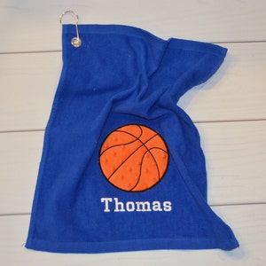 May include: Blue golf towel with an orange basketball and the name "Thomas" embroidered in white.