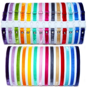 Peut inclure: Un présentoir de 20 colliers en ruban de velours de différentes couleurs, dont le violet, la lavande, le vert, l'orange, le jaune, le turquoise, le rose, le rouge, le gris, le beige et le bleu. Les colliers sont disposés en deux rangées sur un fond blanc.