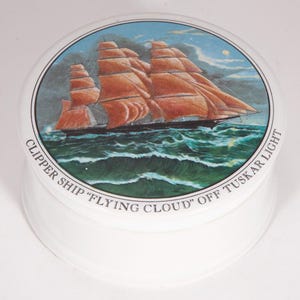Puede incluir: Contenedor de cerámica blanco con tapa que presenta una ilustración detallada de un velero clipper con velas naranjas sobre un mar ondulado bajo un cielo azul. El texto "CLIPPER SHIP 'FLYING CLOUD' OFF TUSKAR LIGHT" está impreso en el borde.