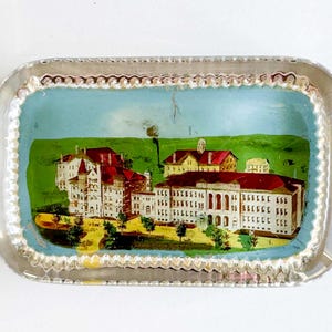 May include: Rectangular glass tray with a silver rim. The tray features a painted scene of a university campus with white buildings, red roofs, and green lawns under a blue sky. A decorative item.