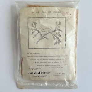Może przedstawiać: Zestaw do szycia poduszki na szpilki z ptakiem w przezroczystej plastikowej torbie. Zestaw zawiera nadrukowany lniany wzór ptaka na gałęzi, instrukcje i nić. Gotowy rozmiar to około 10 cm x 11,4 cm. Od Jane Snead Samplers.