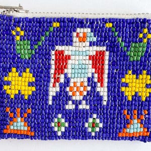 May include: A beaded coin purse with a blue background and a central design of a white bird with red wings. The purse features yellow star-like shapes, green leaf-like shapes, and orange and blue geometric patterns. It has a silver zipper.