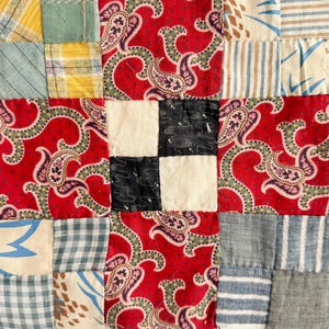 Puede incluir: Primer plano de un textil de patchwork con una variedad de telas estampadas. El diseño incluye paisley rojo, cuadrados blancos y negros, y patrones a cuadros y rayas. El textil es una mezcla de colores y texturas.
