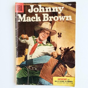 Puede incluir: Portada de cómic vintage de Dell con Johnny Mack Brown. La portada muestra a un vaquero con camisa blanca, pañuelo rojo y sombrero de vaquero. El fondo es amarillo y marrón descolorido.