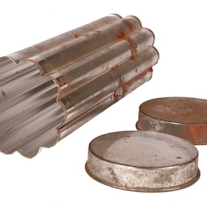 May include: An antique, fluted metal tube pan with two oval lids. The pan is silver-colored with a scalloped edge and shows signs of rust. The lids are also metal and show rust.