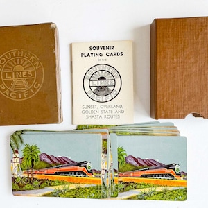 Puede incluir: Juego de cartas Southern Pacific Lines vintage. La caja y el folleto presentan el logotipo de Southern Pacific. Las cartas representan un tren con un paisaje de montaña y palmeras. El juego incluye una caja, un folleto y una baraja de cartas.