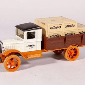 May include: A vintage toy truck in cream, orange, and brown, with a black roof. The truck bed is loaded with wooden crates, each labeled "Caterpillar." The truck has orange wheels and a detailed front end.