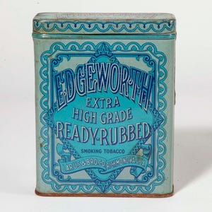 May include: A rectangular, vintage Edgeworth tobacco tin. The tin is light blue with a turquoise central panel featuring the text "Edgeworth Extra High Grade Ready-Rubbed Smoking Tobacco." The design includes ornate scrollwork and the text "Larus & Bro. Co. Richmond, USA."