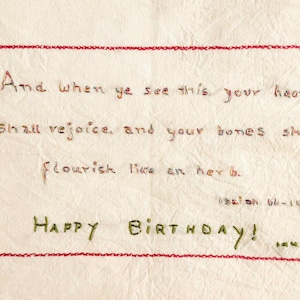 以下が含まれることがあります： 赤いステッチの縁取りとテキストが入った白い布のカード。テキストは「これを見るとき、あなたの心は喜び、あなたの骨は草のように栄えるでしょう。お誕生日おめでとう！」と書かれています。