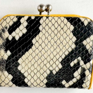 Pode incluir: Uma pequena carteira retangular com fecho de encaixe. A carteira apresenta um padrão de pele de cobra em preto e creme, com uma borda amarela brilhante. O fecho é prateado.