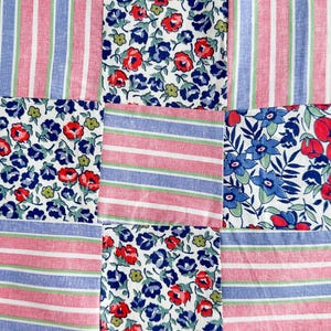 Könnte beinhalten: Ein Patchwork-Textil mit neun Stoffquadraten. Die Quadrate wechseln sich ab mit rot-blauen Streifenmustern und floralen Mustern mit roten und blauen Blumen auf weißem Grund. Der Stoff hat einen rohen Rand.