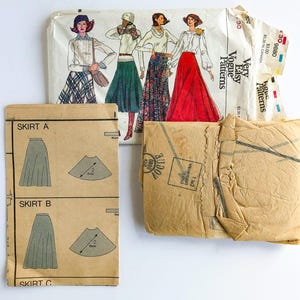 May include: A vintage Very Easy Vogue sewing pattern envelope featuring illustrations of four different skirt styles, accompanied by two tan paper instruction sheets. The envelope displays the number 9880 and shows various skirt designs including plaid, solid, and floral patterns.