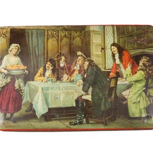 May include: Vintage rectangular tin with a painted scene of a gathering. A woman carries a pie, while several figures sit at a table. The tin has a red border and a slightly distressed appearance, suggesting age.