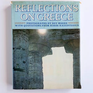 Könnte beinhalten: Ein Vintage-Buch mit dem Titel "Reflections on Greece" mit hellblauem Einband. Der Einband zeigt den Titel in Weiß und den Namen des Autors. Das Bild auf dem Einband zeigt antike griechische Säulen.