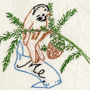 May include: An embroidery design on off-white fabric featuring a light brown bird perched on a green pine branch with a brown pinecone. Below the bird is a blue-outlined ribbon banner with the handwritten black text that reads Me.