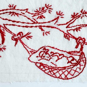 May include: A white fabric panel featuring red thread embroidery of a person resting in a hammock suspended from a tree branch. The design uses simple line work and cross-hatching to depict the figure, the hammock, and the surrounding foliage.