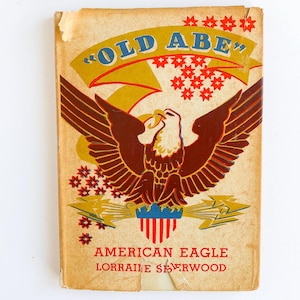 May include: A vintage book cover titled OLD ABE featuring a large brown eagle with spread wings centered on a tan background. The design includes red star patterns, yellow lightning bolts, and a blue and red shield graphic. Text reads AMERICAN EAGLE LORRAINE SHERWOOD.