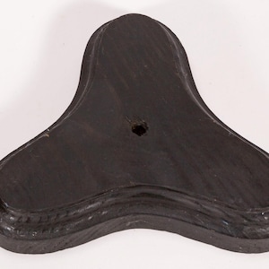 May include: A dark brown, three-lobed wooden base with a carved, curved edge. The base has a hole in the centre and is likely for a decorative item or sculpture. The wood grain is visible.