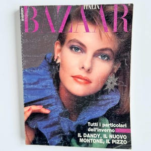 Könnte beinhalten: Ein Vintage-Magazin-Cover von Harper's Bazaar Italia mit einer Person mit braunen Haaren, die ein blaues Kleidungsstück mit Rüschenkragen und sternförmige Ohrringe trägt. Der Text lautet Harper's Bazaar Italia, Tutti i particolari dell'inverno, IL DANDY, IL NUOVO MONTONE, IL PIZZO.