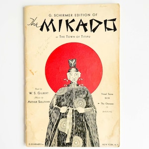 May include: Vintage sheet music cover for "The Mikado or The Town of Titipu." The cover features a black and white illustration of a figure in traditional Japanese attire against a red circle. The title and author names are printed at the top and bottom.