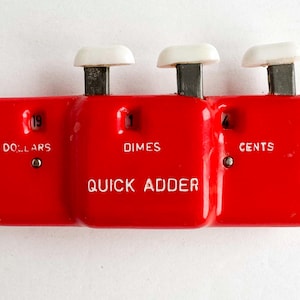 Peut inclure: Un Quick Adder rouge vintage avec trois sections pour les dollars, les dimes et les cents. Chaque section a un bouton blanc et affiche des chiffres. Le mot "QUICK ADDER" est imprimé en blanc sur la section centrale.