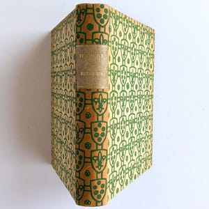 Op de afbeelding: Een vintage boek met een patroon op de kaft. De kaft heeft een herhalend groen ontwerp op een bruinachtige achtergrond. De rug heeft een gouden label met tekst. Het boek staat schuin, met de kaft en rug zichtbaar.