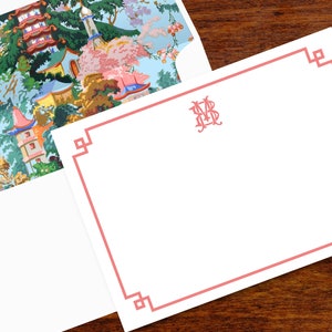 Pode incluir: Conjunto de papelaria branco com borda e monograma rosa. O interior do envelope apresenta uma paisagem colorida de inspira&ccedil;&atilde;o asi&aacute;tica com pagodes e &aacute;rvores. A papelaria est&aacute; sobre uma superf&iacute;cie de madeira escura.