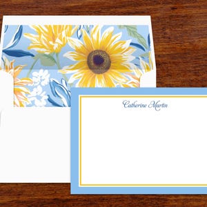 May include: Stationery set featuring a white card with a blue and yellow border, and a matching envelope. The envelope interior displays a floral pattern with sunflowers. The card is inscribed with the name "Catherine Martin".