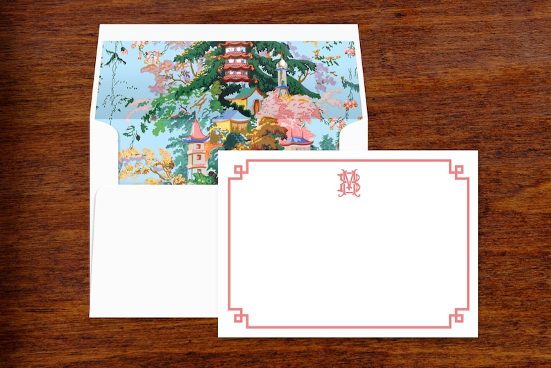 Pode incluir: Um conjunto de papelaria com um cart&atilde;o branco com uma borda coral e um envelope a condizer. O interior do envelope apresenta uma paisagem colorida de inspira&ccedil;&atilde;o asi&aacute;tica com pagodes e &aacute;rvores. O cart&atilde;o tem um monograma no canto superior direito.
