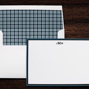 May include: A white stationery set with a teal border and black trim. The stationery includes a matching envelope with a plaid pattern in shades of blue, black, and white. The initials "JMM" are printed in black at the top of the stationery.