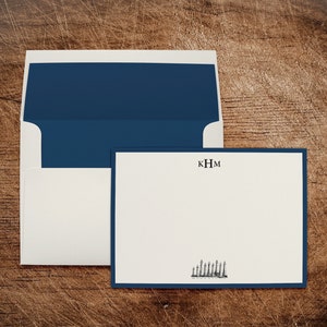 May include: A white card with a navy blue border and a navy blue envelope. The card has a monogram "KHM" and a black and white illustration of a row of lighthouses.