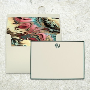 May include: A cream-colored envelope with a colorful abstract design on the inside flap. A cream-colored stationery card with a dark green border and the monogram "MMJ" in a circle in the top center.