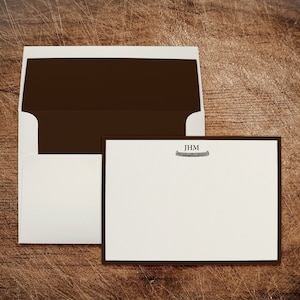 May include: A white envelope with a brown flap and a white card with a brown border. The card has the initials "JHM" and a small image of a canoe.