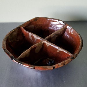 May include: A brown ceramic divided dish with four sections. The dish has a rustic, handmade look and is glazed in a brown and orange color.