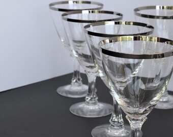 May include: Five clear glass wine glasses with a silver rim. The glasses are arranged in a row on a black surface.