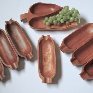 Pode incluir: Conjunto de sete tigelas de servir de madeira, incluindo uma tigela em forma de folha com três seções e seis tigelas longas e estreitas. As tigelas são todas de madeira marrom escura e têm um acabamento liso e polido.