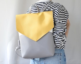 May include: A gray and yellow leather backpack with a flap closure. The backpack has a white stripe on the front.