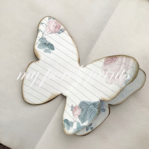 Puede incluir: Una artesan&iacute;a de papel en forma de mariposa decorativa con un patr&oacute;n floral y un dise&ntilde;o de papel rayado. La mariposa est&aacute; doblada por la mitad y tiene una est&eacute;tica vintage.