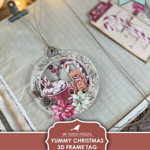May include: Printable 3D Christmas frame tag with a red mug, gingerbread man, candy canes, and poinsettia flowers. The tag is designed to be cut out and assembled into a 3D ornament.